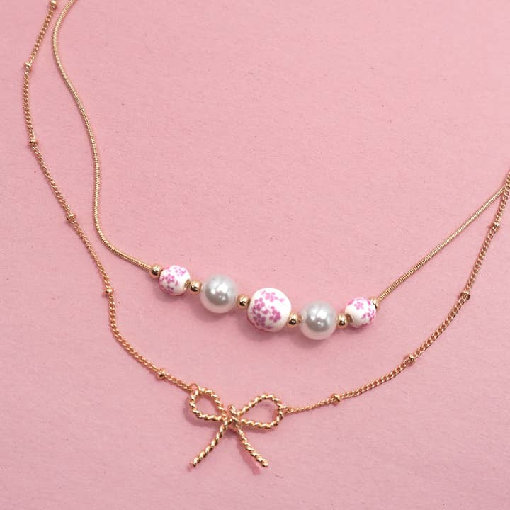 Gold PINK CERAMIC PORCELAIN PEARL BOW LAYER NECKLACE | 80N91556 for wholesale on Faire1