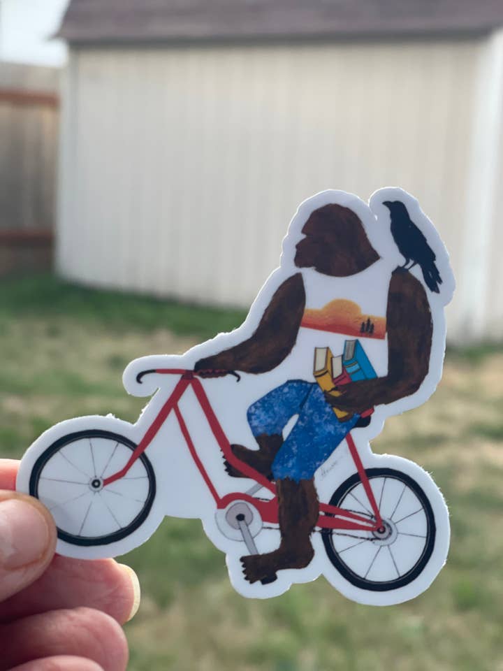 Autocollant Bigfoot à vélo avec livres et corbeau – Autocollant en vinyle fantaisiste Sasquatch découpé pour la vente par Color Crumbs Club