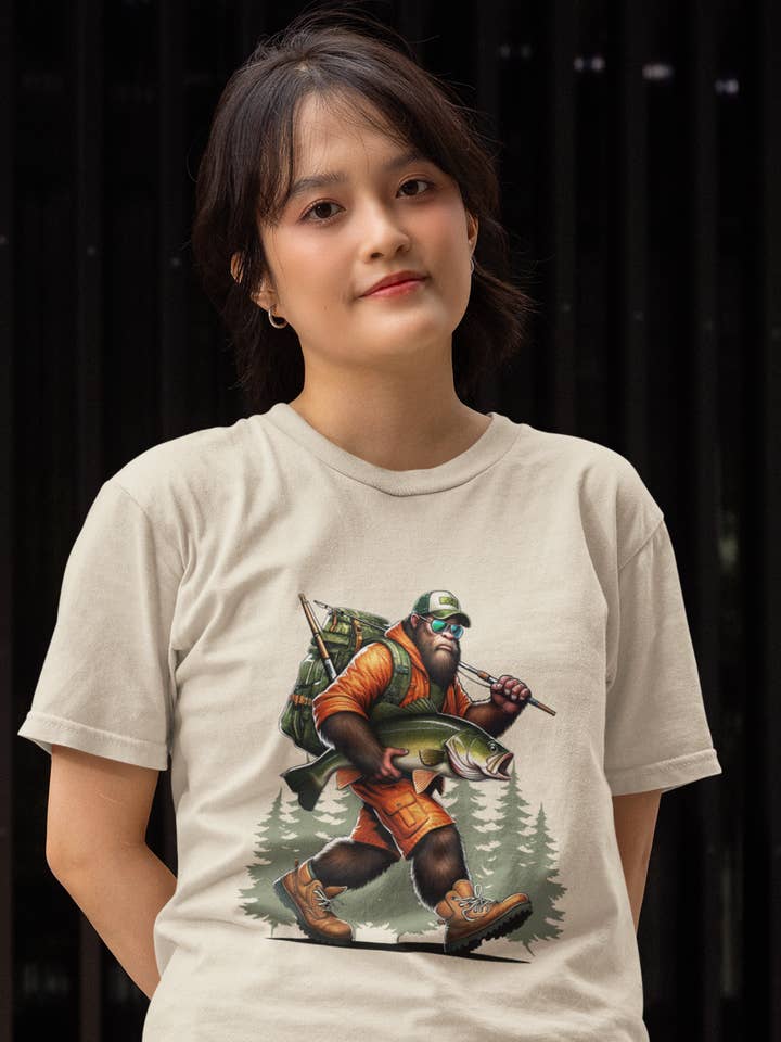 Fishing Bigfoot carrying fish t-shirt (tan) for wholesale by Squatchin’ Country