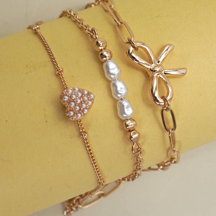 Gold CHARM BRACELET-MULTI LAYER BOW PERAL HEART CHARMS | 80B1317 for wholesale on Faire