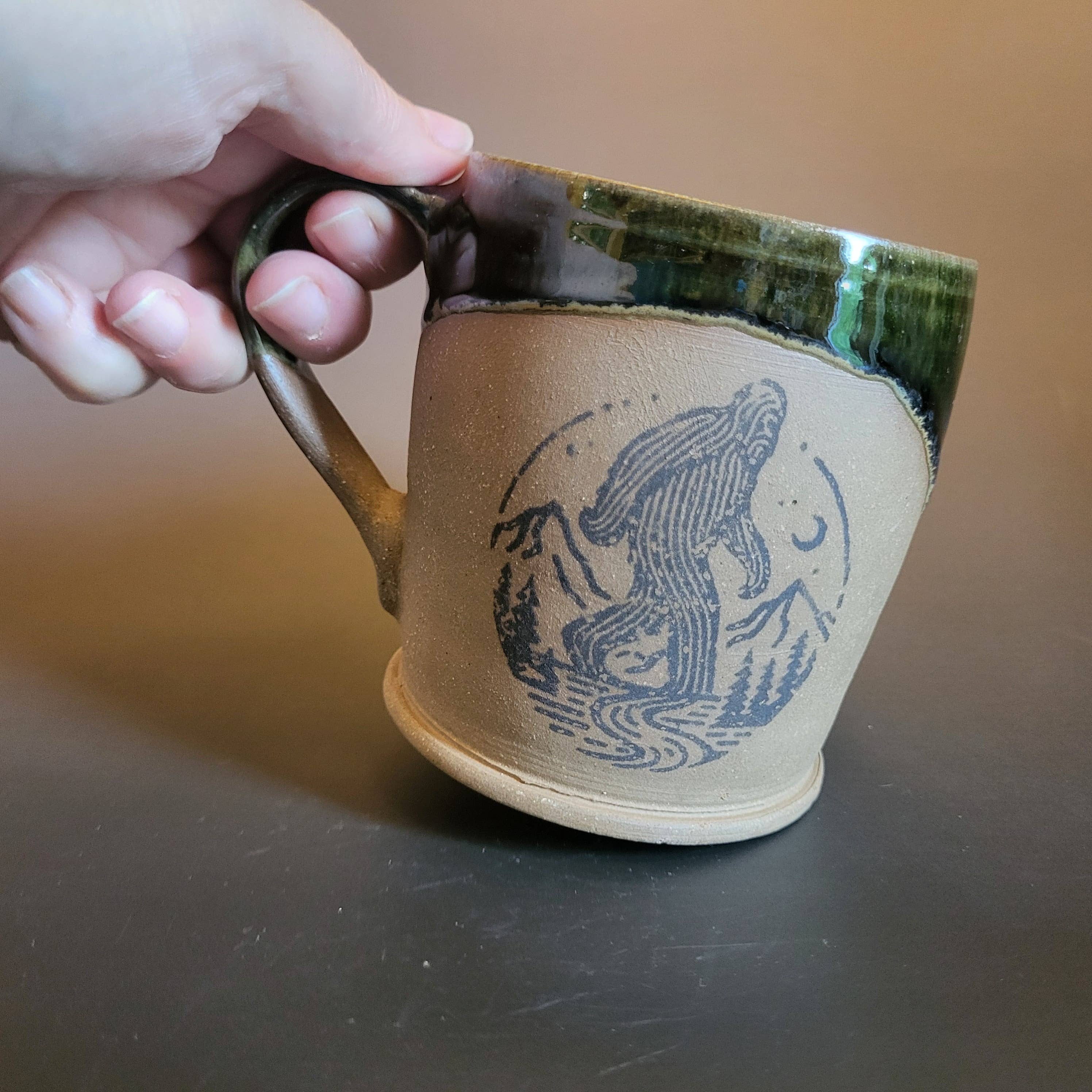 Divine Vessels Pottery - Vente Tasse à café - Emblème stylisé de Bigfoot avec glaçure vert foncé1