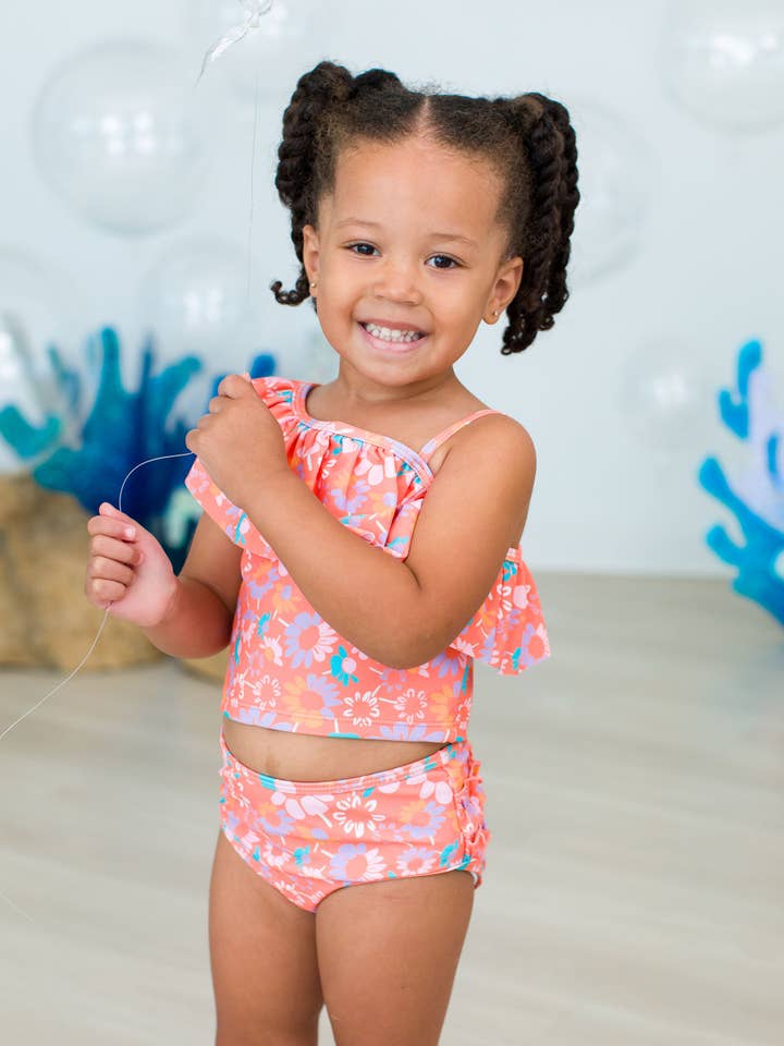 Bañador de dos piezas tipo tankini con volantes traseros característicos y un solo hombro con volantes florales coral para niñas. para venta al por mayor de RuffleButts + RuggedButts