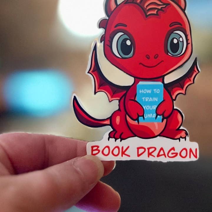 Pegatina de Dragón de Libro | Lindo Dragón Rojo Sosteniendo el Libro ‘Cómo Entrenar a tu Humano’ | Pegatina Impermeable Troquelada para Lectores y Amantes de la Fantasía para venta al por mayor de Tomes and Troves, LLC