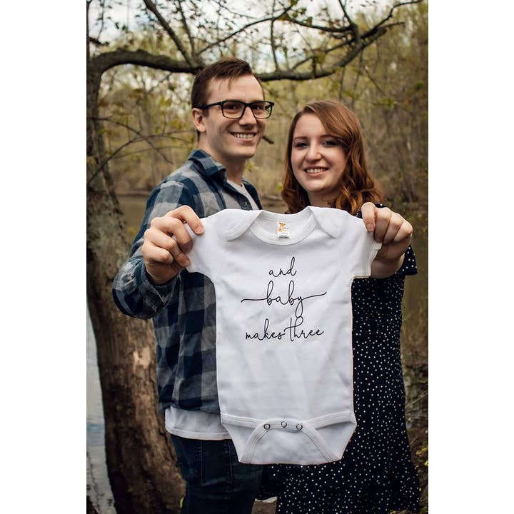 And Baby Makes Three Pregnancy Announcement Onesie for wholesale by Bump & Beyond Designs