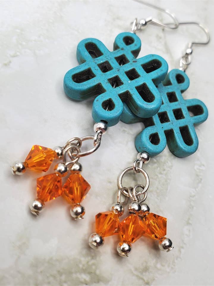 Orecchini a forma di nodo celtico in magnesite tinta turchese con pendenti in cristallo Swarovski arancione per la vendita all'ingrosso da parte di Simply Raevyn
