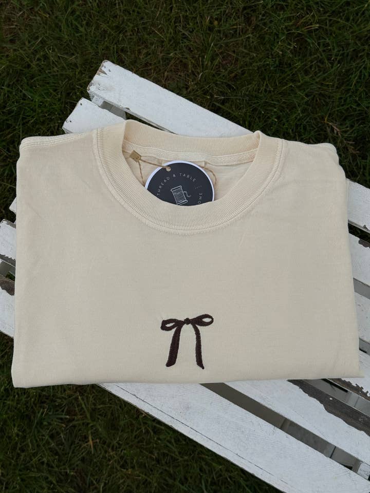 T-shirt ivoire brodé d'un nœud marron chocolat pour la vente par Thread & Table
