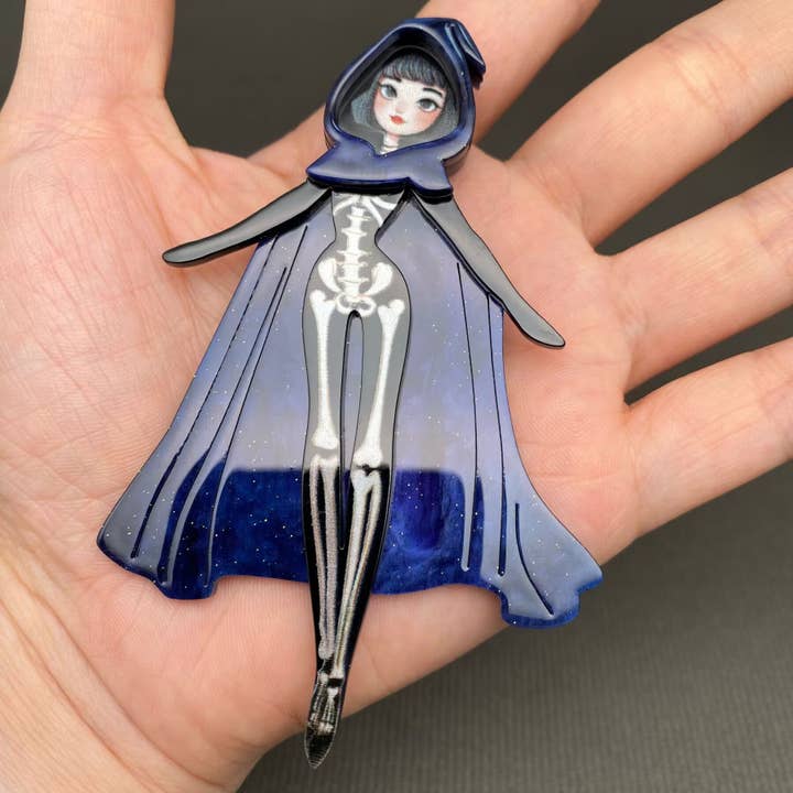 Broche en acrylique de sorcière squelette portant une cape pour la vente par Mio Queena