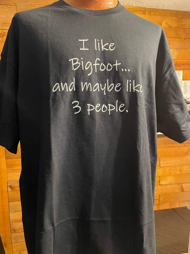 T-shirt Mi piace Bigfoot (nera) per la vendita all'ingrosso da parte di Squatchin’ Country