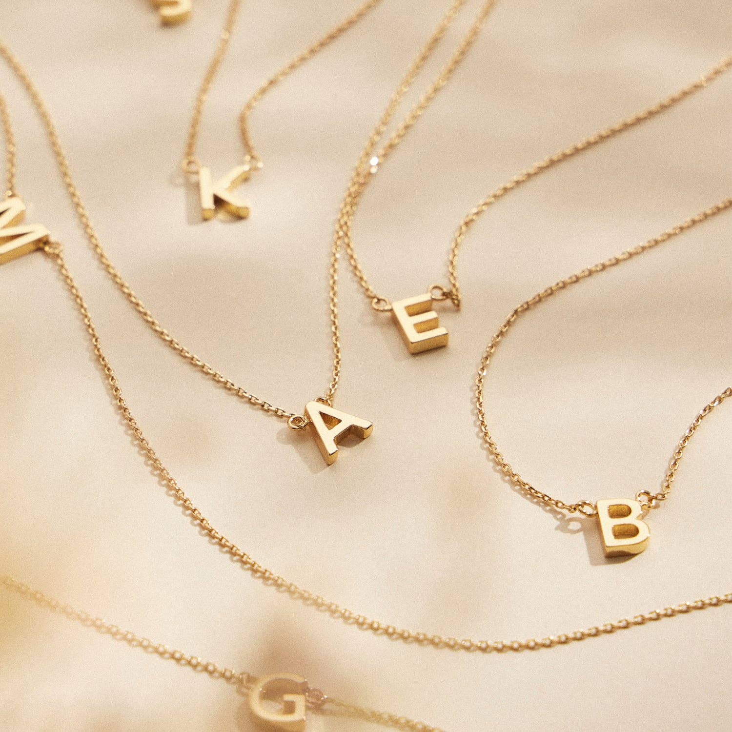 16 ACTIVOS Paquete de 16 collares dorados con abalorios metálicos con letras iniciales de venta al por mayor en Faire1