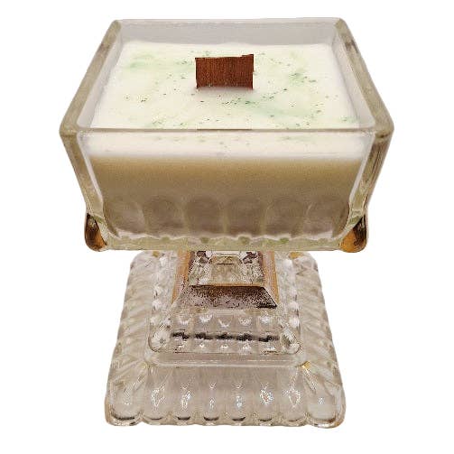 Candela in cera di soia con stoppino in legno su piedistallo di vetro Jeanette chiaro e dorato. per la vendita all'ingrosso da parte di Beloved Bijou Adornments and Apothecary