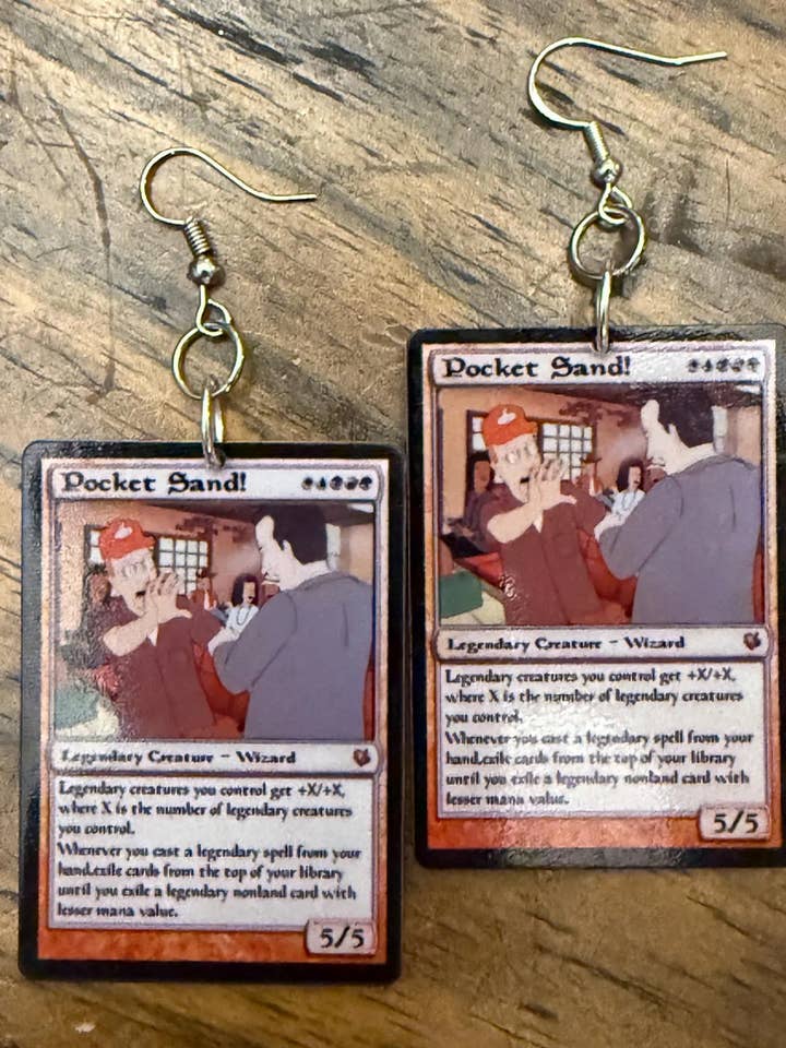 Orecchini in acrilico con carta magica "SABBIA IN TASCA!" di King Of The Hill per la vendita all'ingrosso da parte di Luna Luma Design