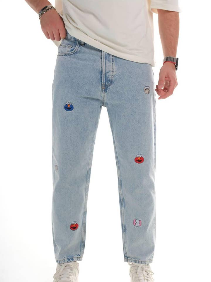 Jeans in denim azzurro chiaro a vestibilità comoda da uomo con divertenti toppe ricamate di cartoni animati 0525C1397 per la vendita all'ingrosso da parte di Monocloth