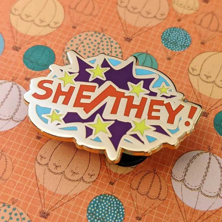 She/They pronouns hard enamel pin for wholesale by Cunning Linguist Co.