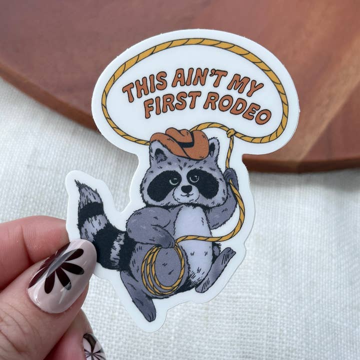 This Ain't My First Rodeo Cowboy Raccoon Lasso Sticker for wholesale by Big Moods