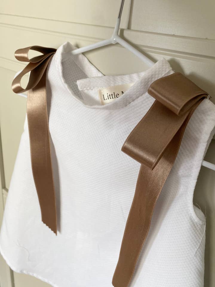 Jesusito i hvid piqué med bånd på skuldrene for engroshandel hos Littlemanuela