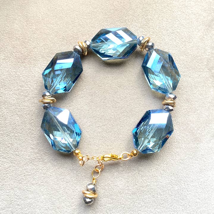 Bracciale elastico dorato con cristalli blu sfaccettati grandi. per la vendita all'ingrosso da parte di Marble Designs Jewelry