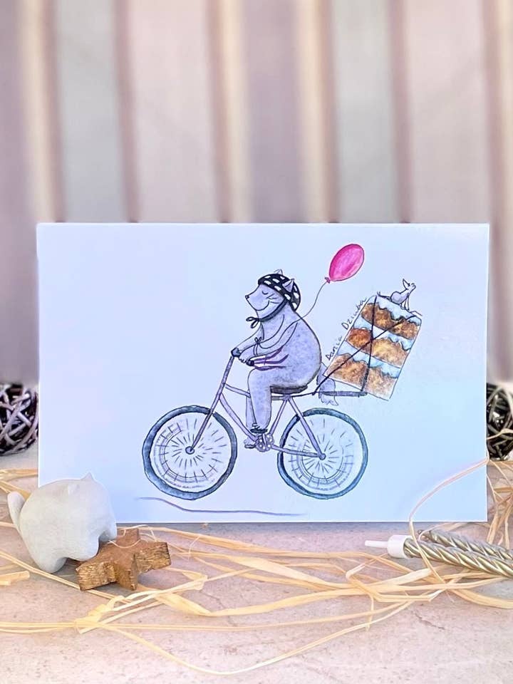 Cat riding bicycle with cake: Greeting card for wholesale by Dariia Dziuba