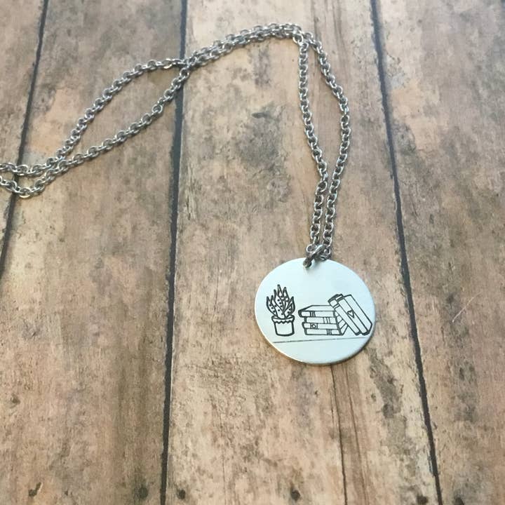 Stack of books with plant circular pendant in silver color for wholesale by Jamie Haley Designs