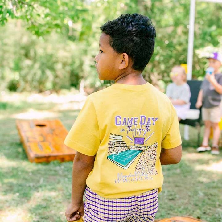 Game Day in the South | Purple + Gold | Football Kid’s Tee for wholesale by Magnolia Mudbugs