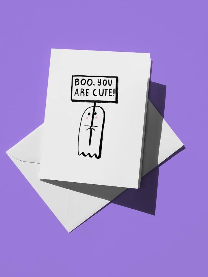 Schattig spook met een bordje "Boe, je bent schattig" A2 wenskaart Halloween griezelig minimalistisch handgetekende humor herfst grappige woordspeling oktober vakantie voor wholesale door semiserious studio